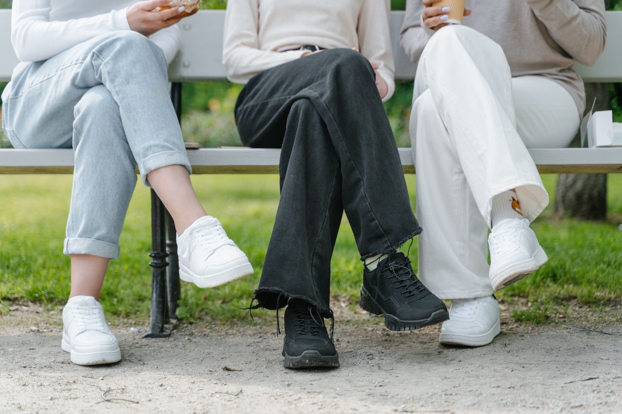 Three people sitting casually on a park bench with crossed legs and casual wear.